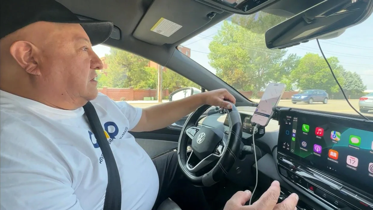 Man driving a Volkswagen electric vehicle using COOP Drivers navigation on dashboard screen and smartphone mount.