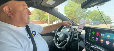 Man driving a Volkswagen electric vehicle using COOP Drivers navigation on dashboard screen and smartphone mount.