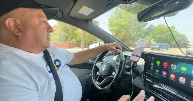 Man driving a Volkswagen electric vehicle using COOP Drivers navigation on dashboard screen and smartphone mount.