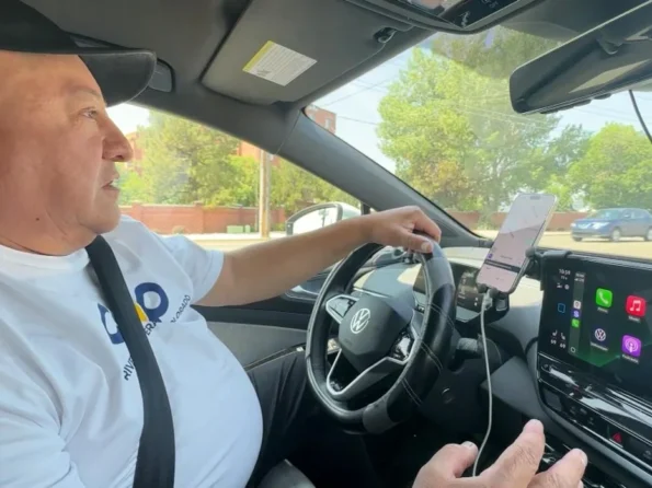 Man driving a Volkswagen electric vehicle using COOP Drivers navigation on dashboard screen and smartphone mount.